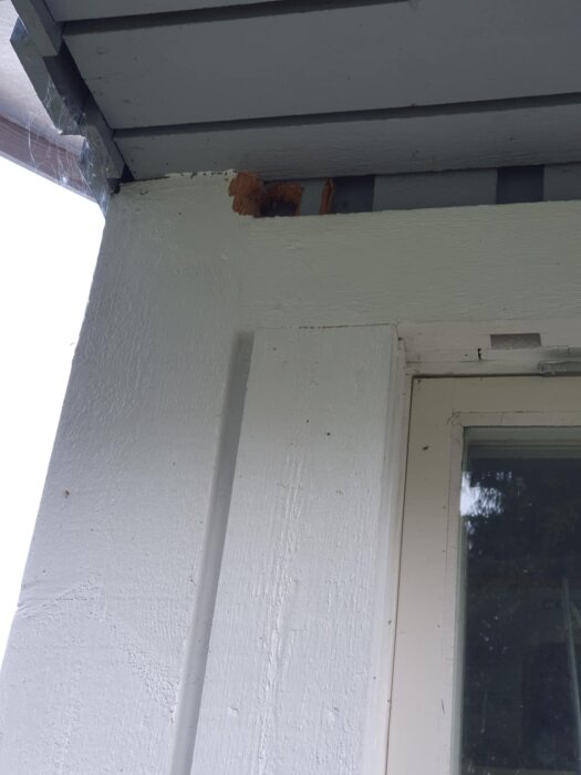 Hörn av en byggnad med vitmålat trä och skadat område nära taket.