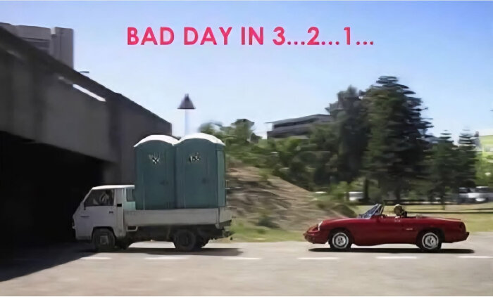 En lastbil med två bajamajor kör mot en låg viadukt medan en röd sportbil kör bredvid. Texten "BAD DAY IN 3...2...1..." finns ovanför.