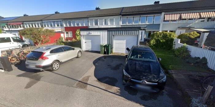 Radhuslänga med två bilar parkerade framför, omgiven av buskar och ett cykelställ i ett bostadsområde.