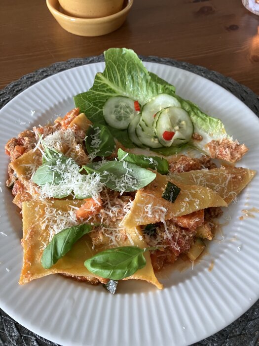 One pot lasagne med basilika och riven ost på tallrik, serverad med sallad och inlagd gurka.