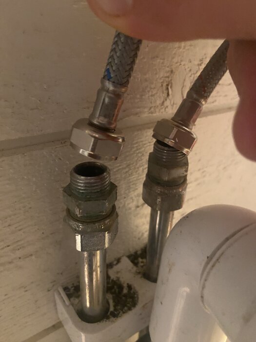 Flexibla metallslangar och kopplingar på vattenrör i ett fritidshus under installation av en ny blandare, visar storleksproblem med gängor.