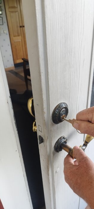 En hand vrider en nyckel i ett gammalt dörrlås på en vit träyta. Dörren är något öppen.