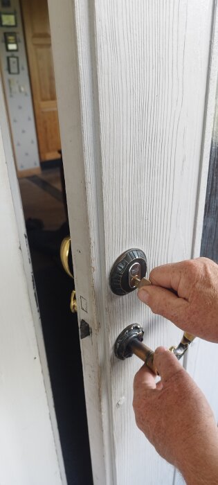 En hand vrider en nyckel i ett gammalt dörrlås på en vitmålad ytterdörr.