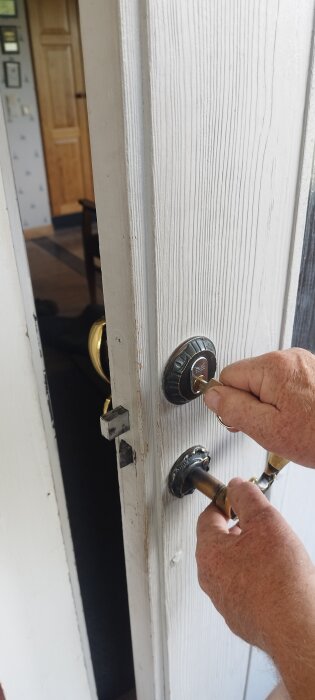 Man försöker vrida en nyckel i ett äldre dörrlås som verkar kärva, på en vitmålad dörr med guldfärgat handtag.