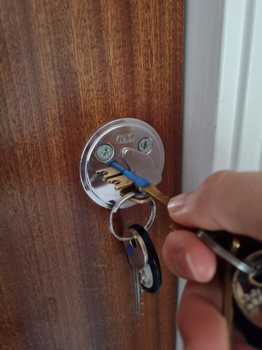 Nyckel med nyckelring insatt i dörrlås, fast i specifik position.