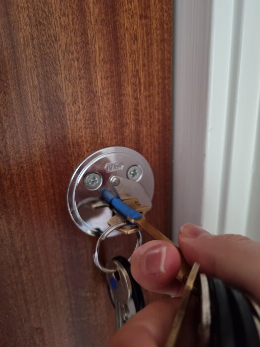 Nyckel instoppad i ett dörrlås på brun trädörr, en hand håller nyckeln.