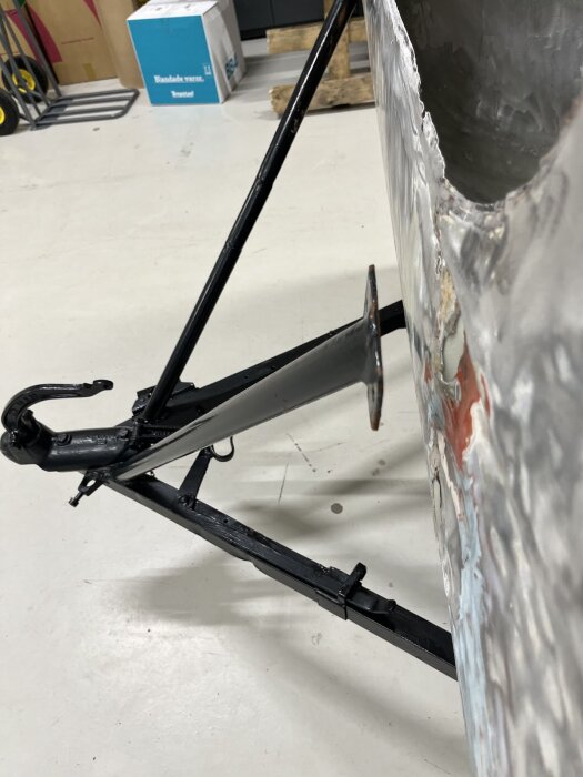 Anslutningsdrag och bucklig plåt på en vagn under renovering i garage, visar avkapade stag och påbörjad reparation av utsidan.