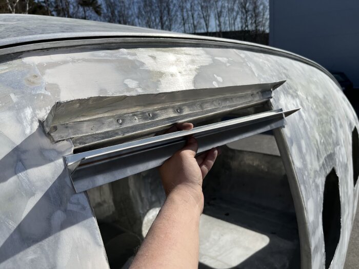 Person installerar en ny dropplist i aluminium ovanför dörren på en renoverad vagn, mot en bakgrund av slipat och spacklat karosserimetall.