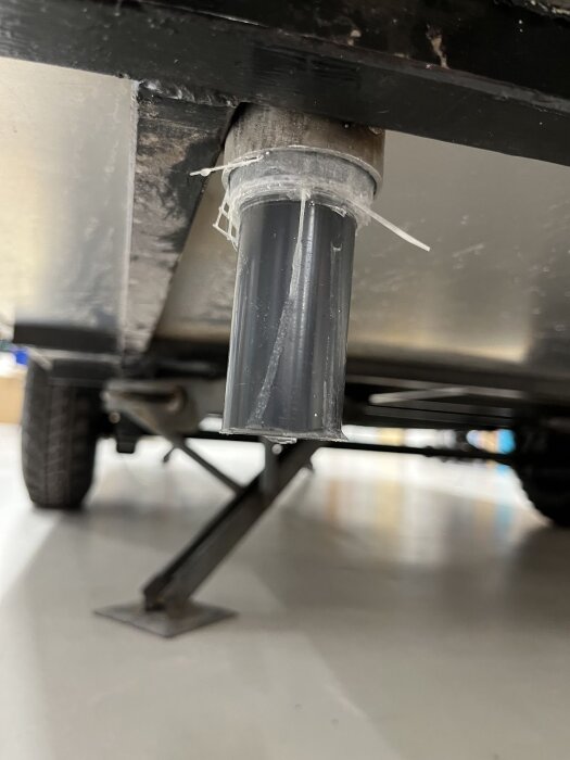 Svetsat avloppsrör under en vagn, med anslutning i metall och plastbeklädnad, för att leda ut vatten effektivt.
