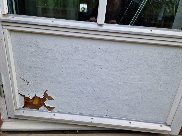 Rötangripen spegel i en altandörr med synlig skada och flagnande yta.