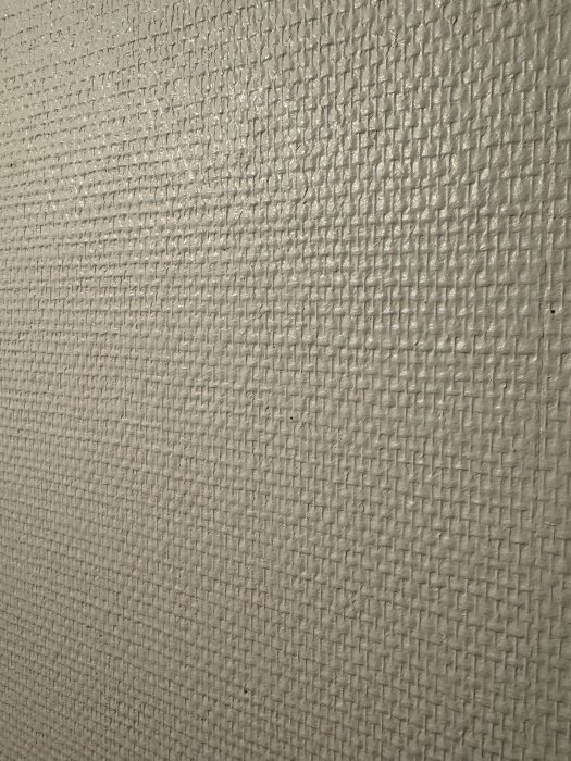 En närbild av glasfiberväv med grovt rutmönster målat i ljus färg, typiskt för interiör från 90-talet.