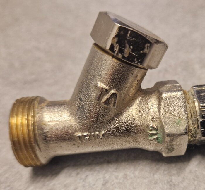 En metallisk returventil med gängad anslutning visas närbild mot en neutral bakgrund.