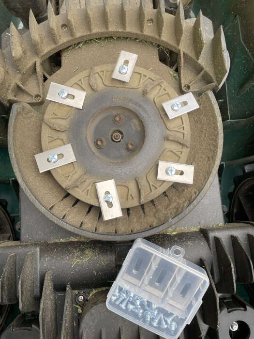 Gräsklipparens knivar bytta och fastsatta med metallbrickor och skruvar. Plastlåda med extra tillbehör synlig. Köpt på Temu.