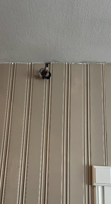 Hoptrasslade kablar syns på en vägg, nära taket, mot en beige, randig panel.