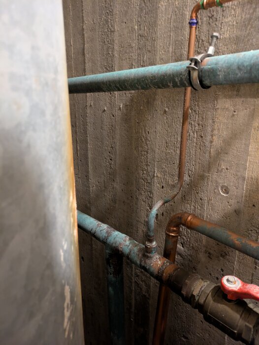 Rostiga koppar- och stålrör i ett hydroformatsystem, kopplade med ventil på betongvägg. Inga backventiler synliga.