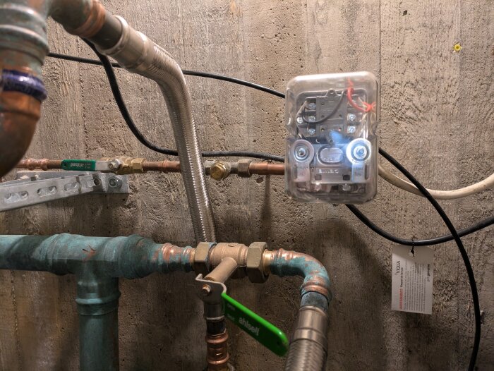 Rörsystem med ventiler och tryckluftskopplare mot en betongvägg, med olika rörmaterial och en delvis öppen elbox.