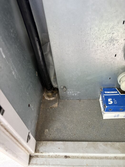 Kabelrör och Tungsram-lampa i ett elskåp med dammig botten.