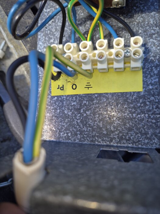 Kopplingsplint med flera anslutna kablar i olika färger, monterad på en gul markeringsremsa med symboler.