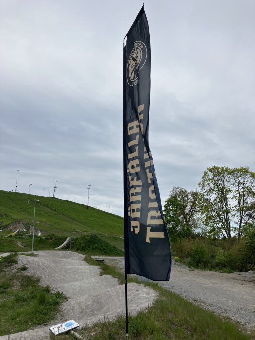 Flagga med texten "Säffle Trial" vid en kuperad, lummig grusbana under molnig himmel.