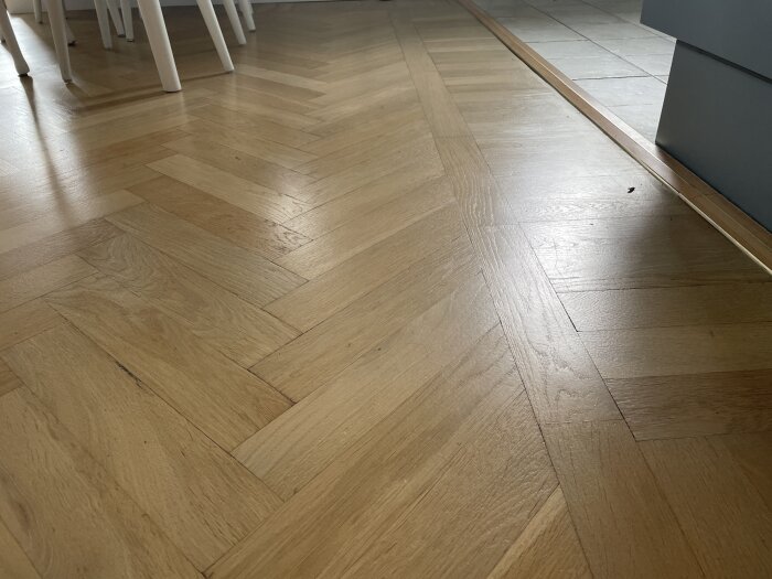 Parkettgolv i fiskbensmönster med ljus träton, delvis slipad ytbehandling; bordben i bakgrunden.