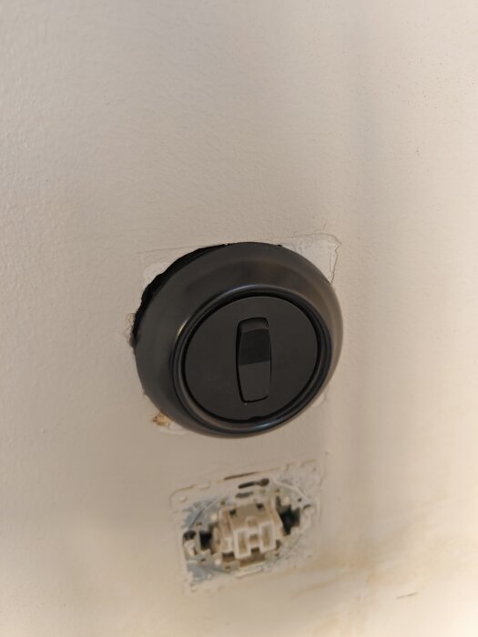 Rund strömbrytare på vit vägg efter byte till Renova, synligt hål efter tidigare fyrkantig dosa.