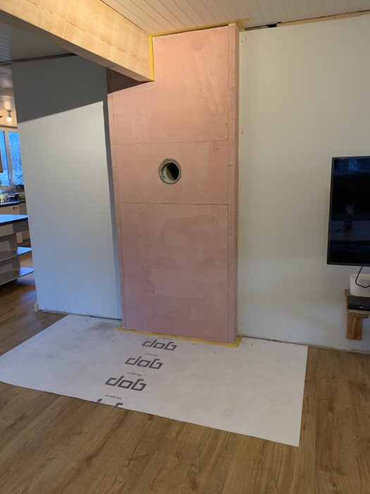 Kamininstallation med vägg av kalciumsilikatskivor och röröppning i ett vardagsrum med trägolv och tak.