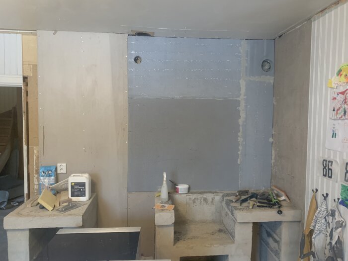 Byggprojekt i kök med rå betongyta, verktyg och byggmaterial synligt; betongprimer använd; saknar spiskåpa.