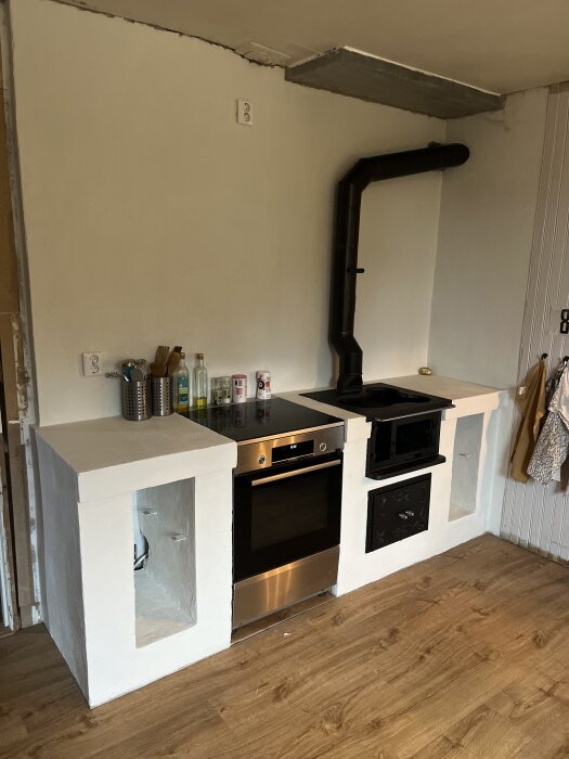 Kök med spis och ugn, betongväggar och trälaminatgolv, spiskåpa saknas; primer från Byggmax använd.