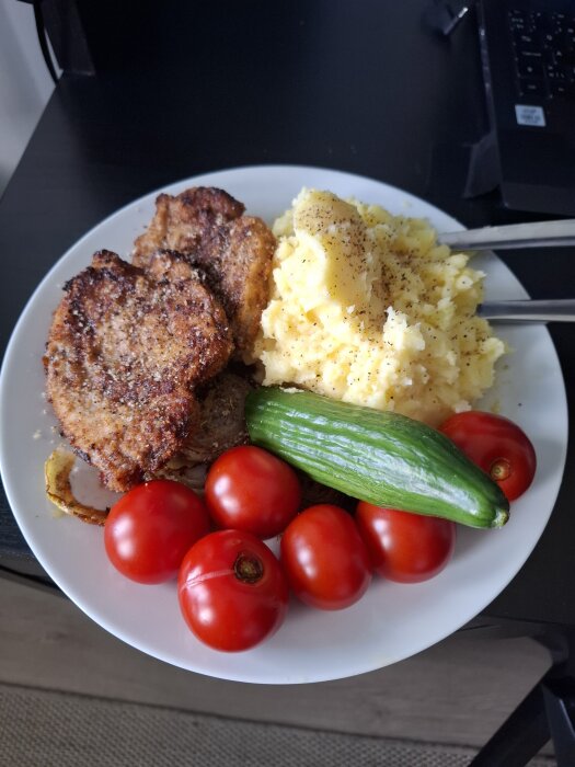 Tallrik med skinkschnitzel, potatismos, tomater och gurka.