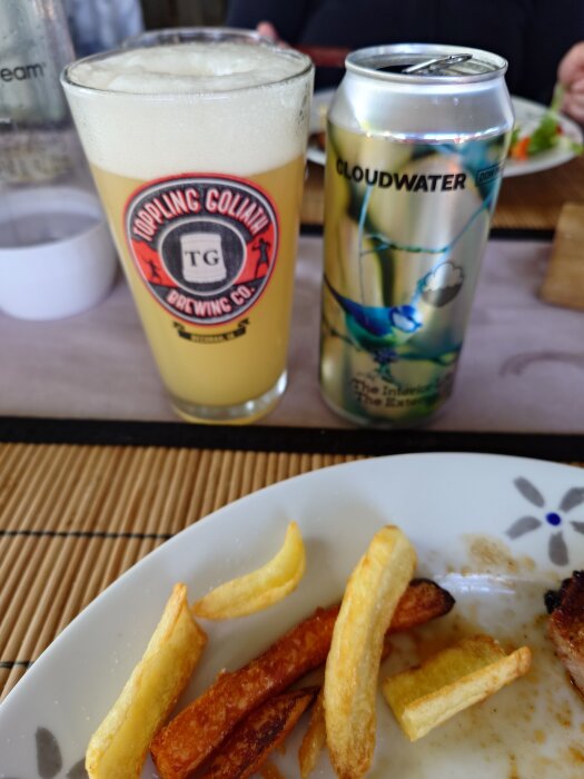 Ett glas med pale ale från Cloudwater bredvid en ölburk och tallrik med pommes frites på ett bord.
