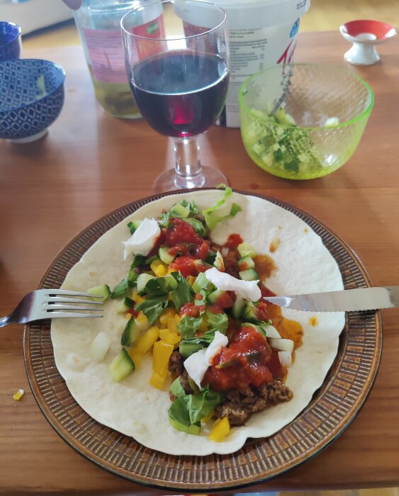 Tacowrap med sallad, gul paprika, köttfärs, ost och salsa på en tallrik med ett glas rödvin.