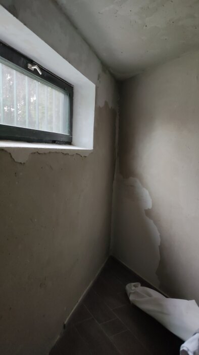 Vägg i inre hörn med ojämn puts och små skador runt fönster, förberedelse inför målning efter renovering och fuktskador.