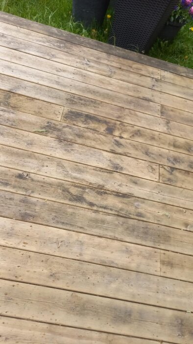 Rengjort träaltandäck med återstående mörka fläckar, omgivande gräsmatta och krukväxter synliga i bakgrunden.