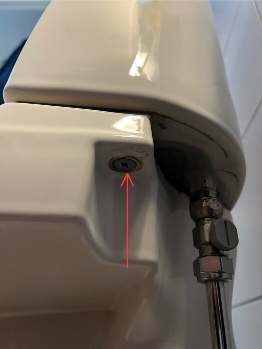 Skruv på sidan av en toalettstol, markerad med röd pil, misstänkt läcka synlig. Fråga om det kan bero på packningen.