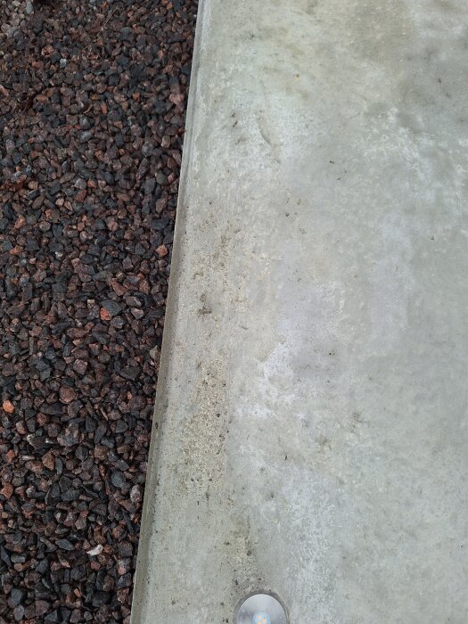 Betongplatta med småhål och ojämnheter bredvid en grusyta.