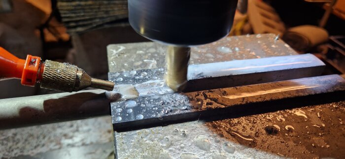 Bilden visar en fräsmaskin i arbete med kylvätska på metallstycket under bearbetning.