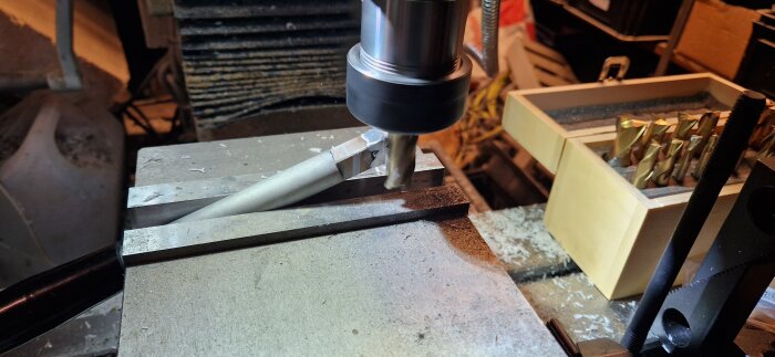 Fräsprocess på en arbetsbänk med verktyg och borrhål, där ett metallhandtag bearbetas efter att ha skadats.