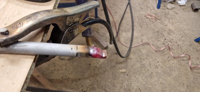 Svetsade handtag på fräs, fastklämt med tving, efter reparation av avbrutet handtag. Verkstadsmiljö på betonggolv.