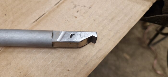 Verktygshandtag av stål med ny svetsskarv, placerat på ett kartongunderlag. Rest från en fräsoperation.