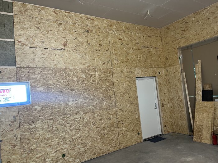 OSB-väggar och gips i högdelen med en vit dörr i ett nybyggt rum.