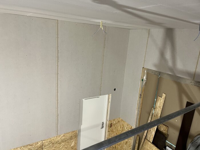 OSB- och gipsskivor monterade på väggar, med dörröppning synlig, i ett rum under konstruktion.