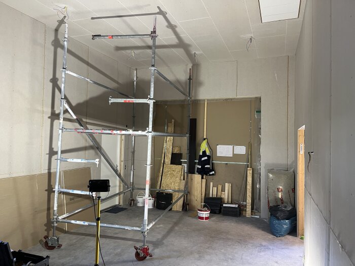 Inomhusbygge med OSB- och gipsskivor, ställning, verktyg och byggmaterial mot en vägg.
