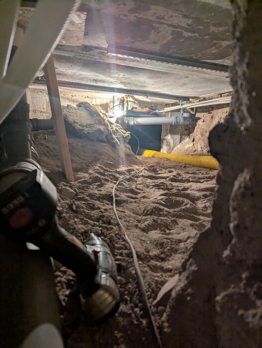 Krypgrund med kablar och verktyg, inklusive borrmaskin, syns i bilden.
