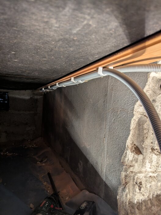 Krypgrund med installerad slang längs väggen, byggmaterial synligt.