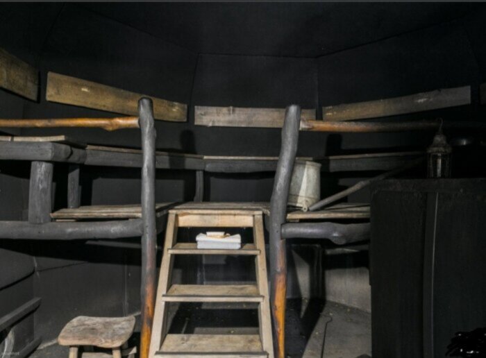 Underjordisk rökbastu med träbänkar, trappsteg och mörka väggar.