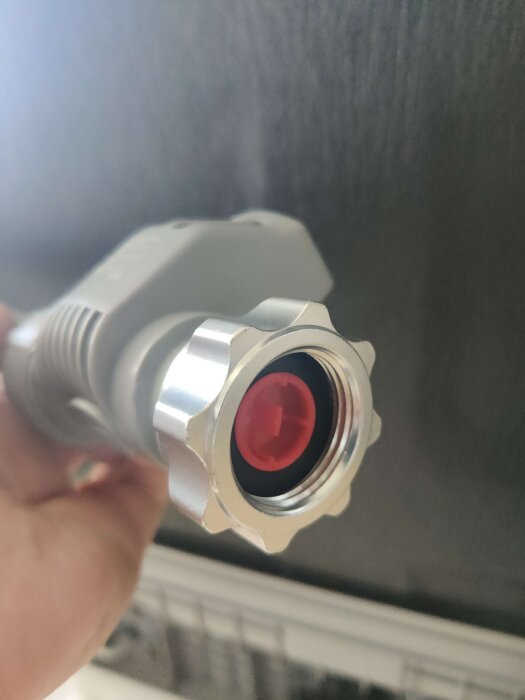 En snabbkoppling för diskmaskin med röd insida visas mot en mörk bakgrund.