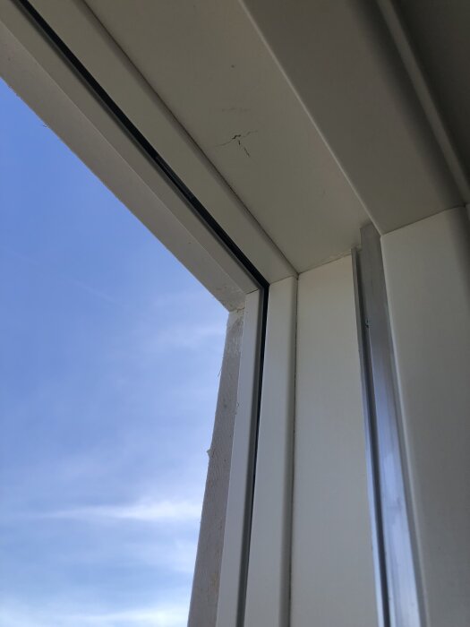 Överkant av ett nyinstallerat vridfönster med synliga sprickor i aluminiumramen, mot en blå himmel i bakgrunden.