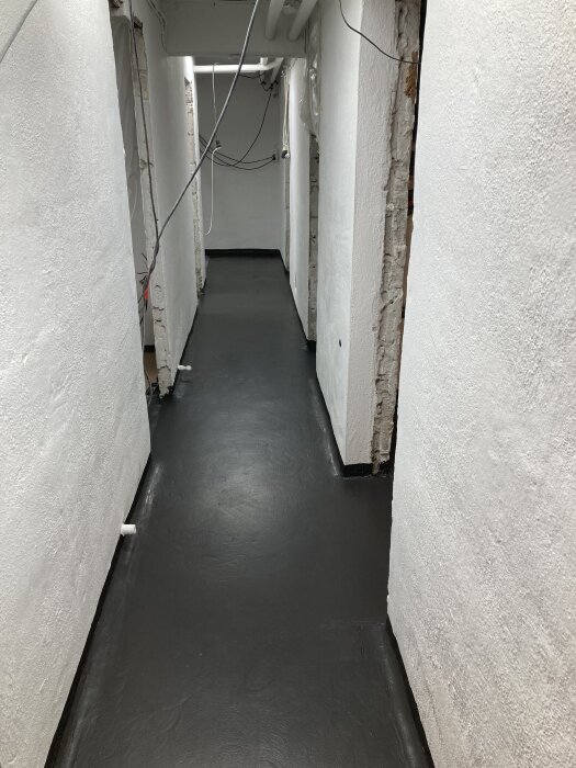 En nymålad korridor med vita väggar och ett mörkt, slipat golv, med synliga kablar i taket.