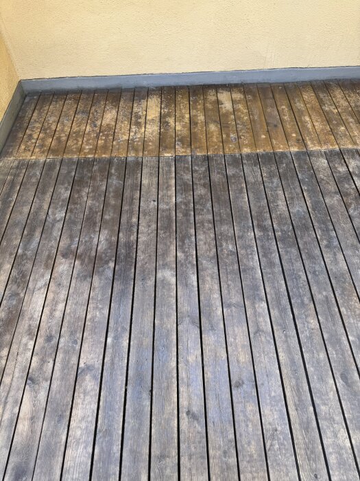 Terrass med trall i olika nyanser, mörkare partier och fläckar synliga efter rengöring och tidigare behandling, bredvid en gul vägg.