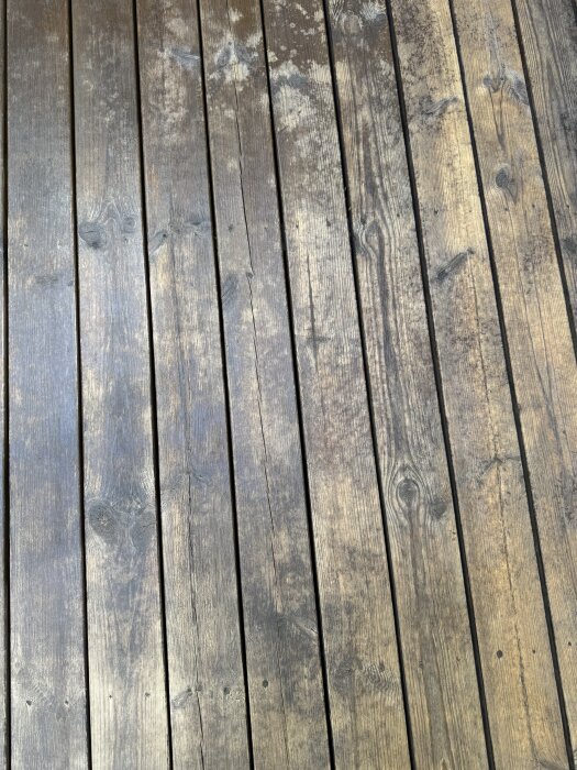 Terrassen visar träplankor med ojämn färg och fläckar efter skrubbning och rengöring, förbereds för oljebehandling för att jämna ut nyanserna.